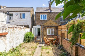 A residential property with a brick house, a white building, and a garden area with a table and chairs. - GuestReady - Charming Kingston Home with Garden (London)
