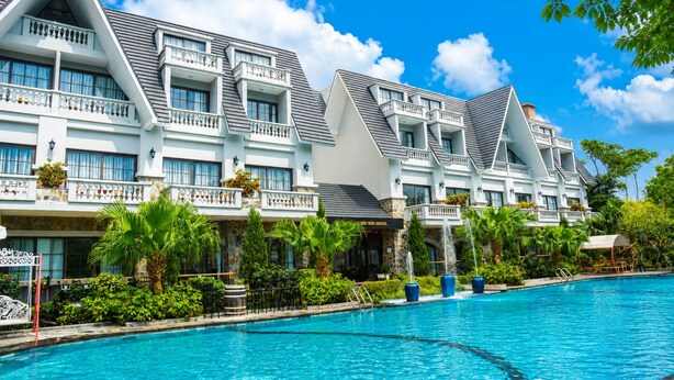 A hotel with multiple balconies, a swimming pool, and lush greenery.