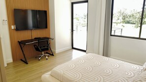 Une chambre comprenant un lit, un bureau avec une chaise, un téléviseur fixé sur un panneau en bois et une porte-fenêtre coulissante donnant sur un espace extérieur.