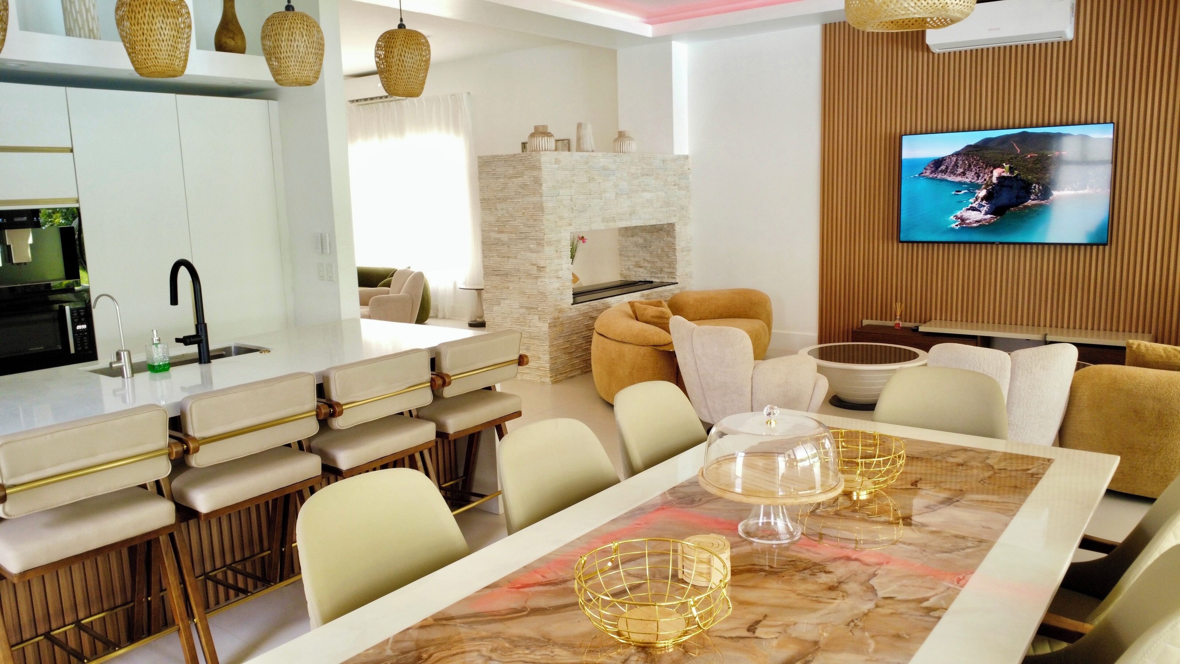 Un salon moderne comprenant un coin repas, une cheminée en pierre et un téléviseur fixé sur un mur recouvert de panneaux en bois.