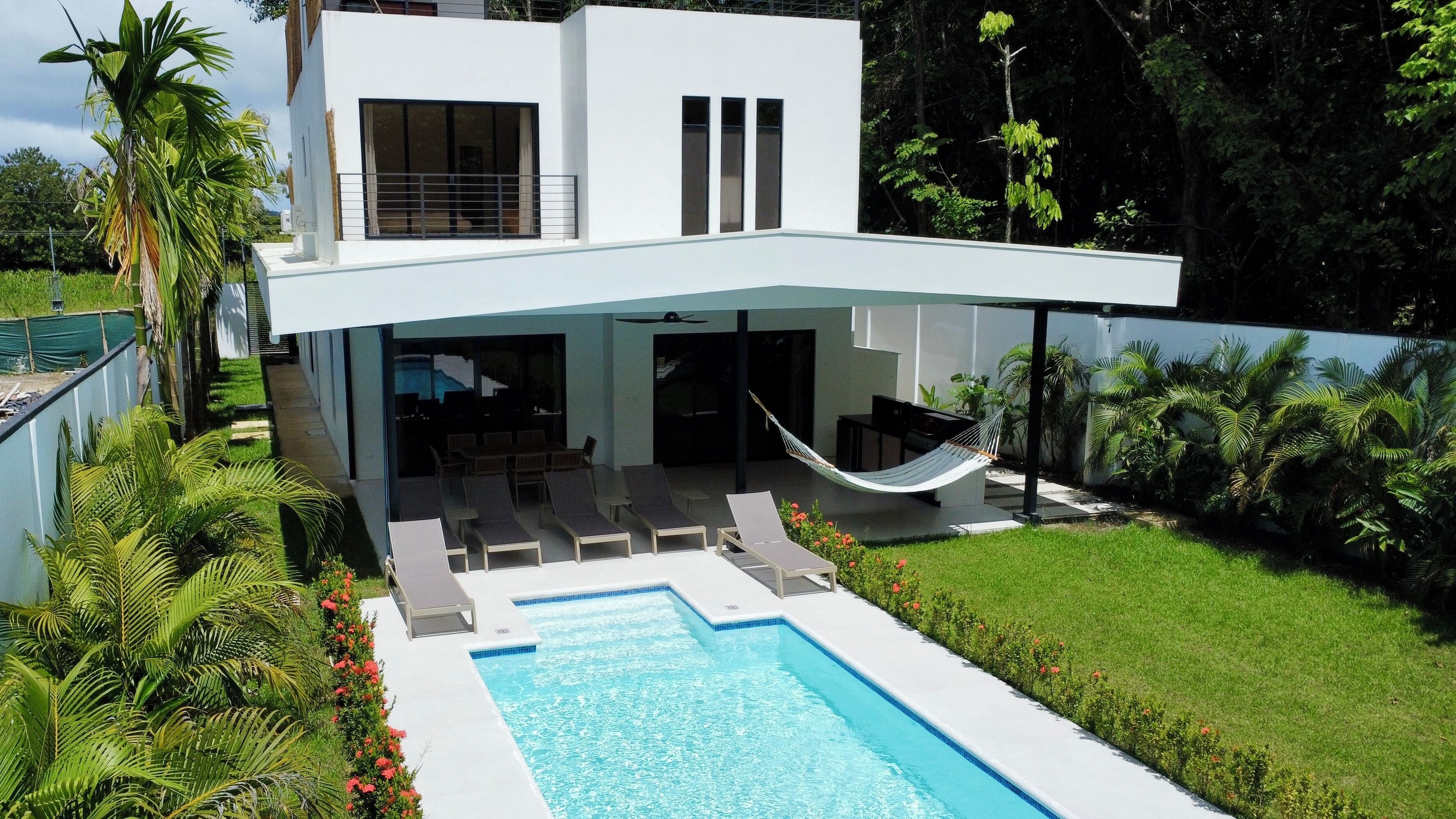 A modern two-story house with a swimming pool, outdoor seating, and a hammock.