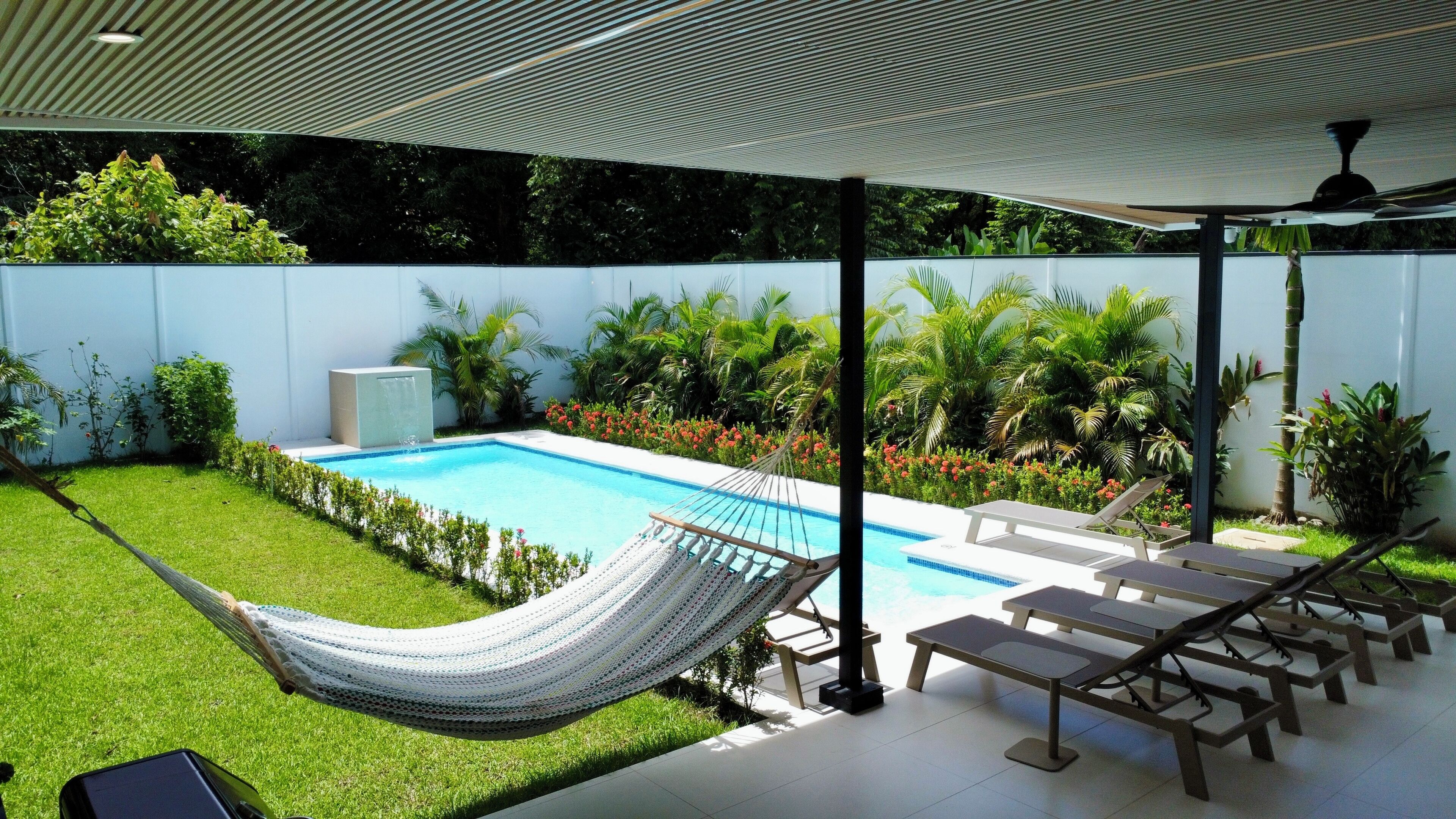 Un área de piscina con una hamaca, sillas de descanso y un porche cubierto.