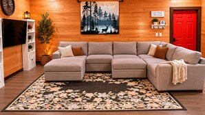 A cozy living room with a sectional sofa, a red door, a wall-mounted TV, and a forest-themed tapestry. - Secluded Cabin Retreat - Fast internet - Fire Pit (Summerville)