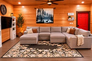 A cozy living room with a sectional sofa, a red door, a wall-mounted TV, and a forest-themed tapestry. - Secluded Cabin Retreat - Fast internet - Fire Pit (Summerville)