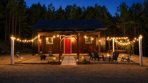 A small wooden cabin with a red door, surrounded by a deck with outdoor seating and string lights. - Secluded Cabin Retreat - Fast internet - Fire Pit (Summerville)
