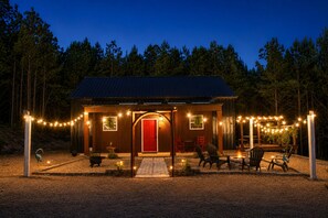 A small wooden cabin with a red door, surrounded by a deck with outdoor seating and string lights. - Secluded Cabin Retreat - Fast internet - Fire Pit (Summerville)