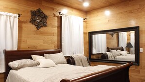 A wooden-paneled bedroom with a large bed, two bedside tables, a mirror, and a wall clock. - Secluded Cabin Retreat - Fast internet - Fire Pit (Summerville)