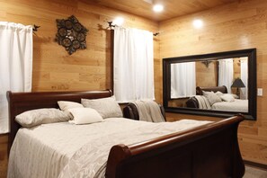 A wooden-paneled bedroom with a large bed, two bedside tables, a mirror, and a wall clock. - Secluded Cabin Retreat - Fast internet - Fire Pit (Summerville)