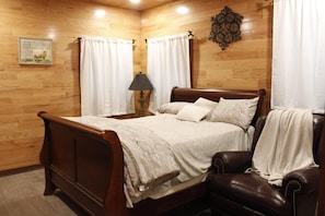 A wooden-paneled room with a bed, a chair, and a lamp.