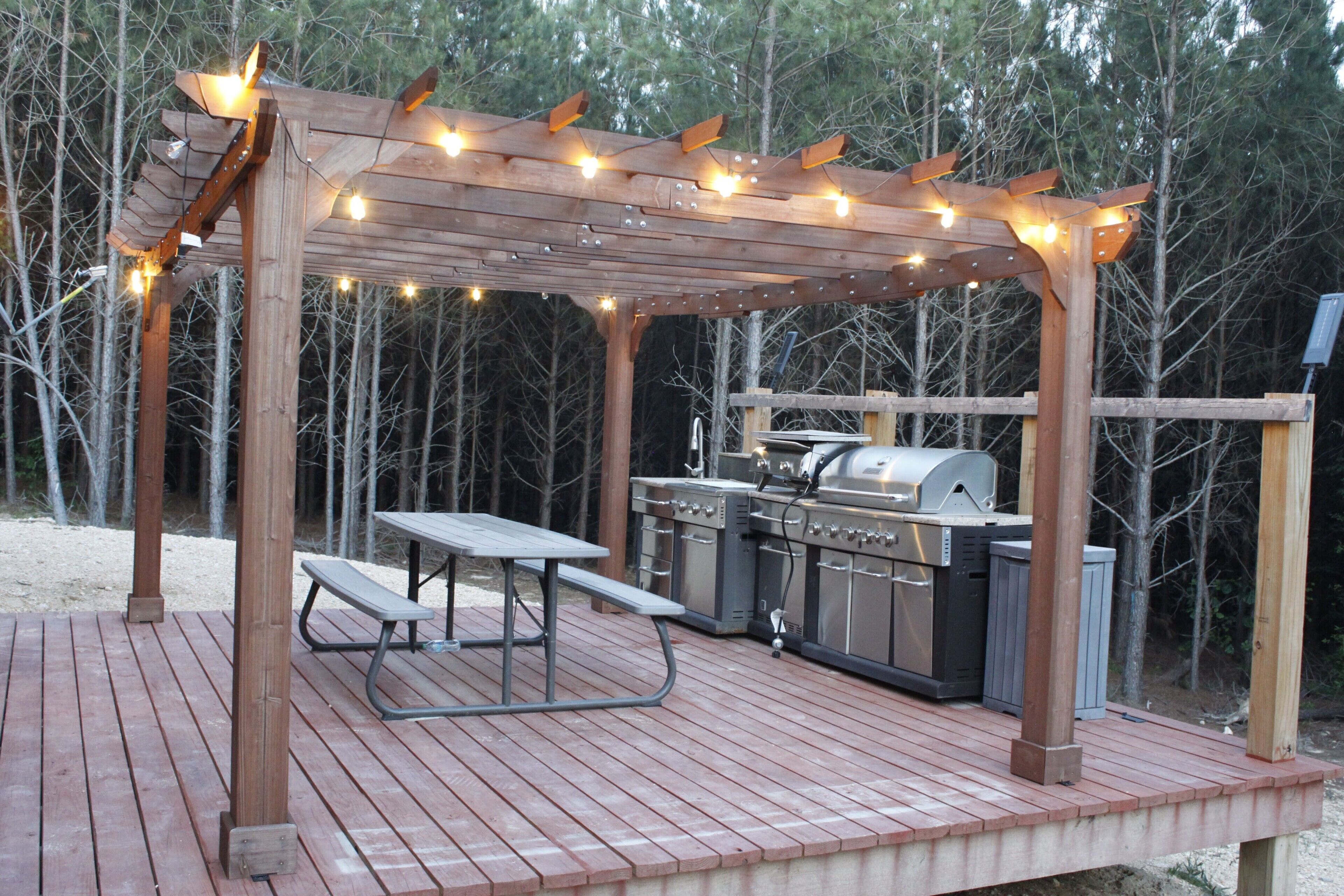 An outdoor wooden deck with a pergola, string lights, a grill, and a picnic table.