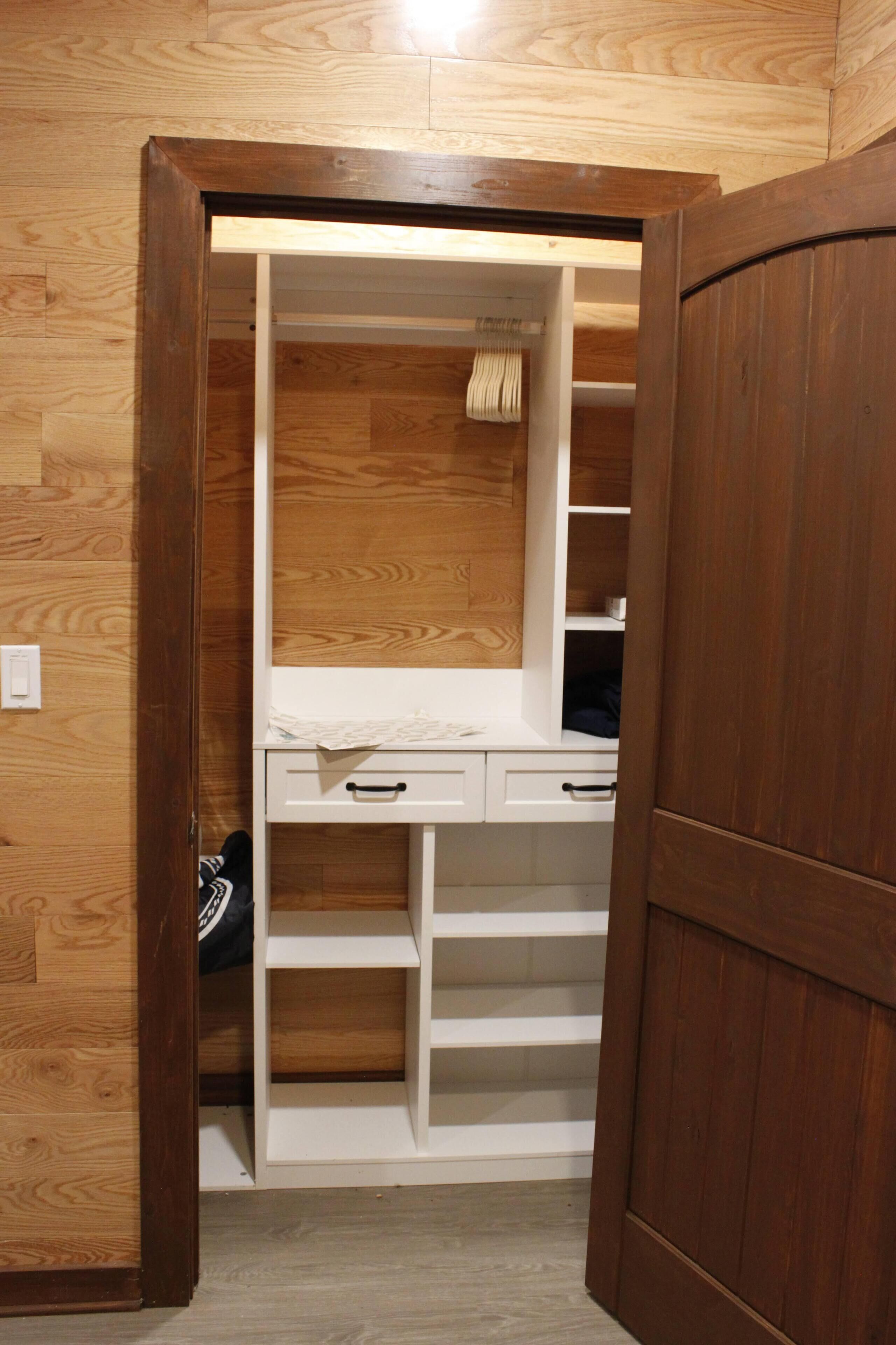 A walk-in closet with wooden flooring, white shelving, and a mirror.