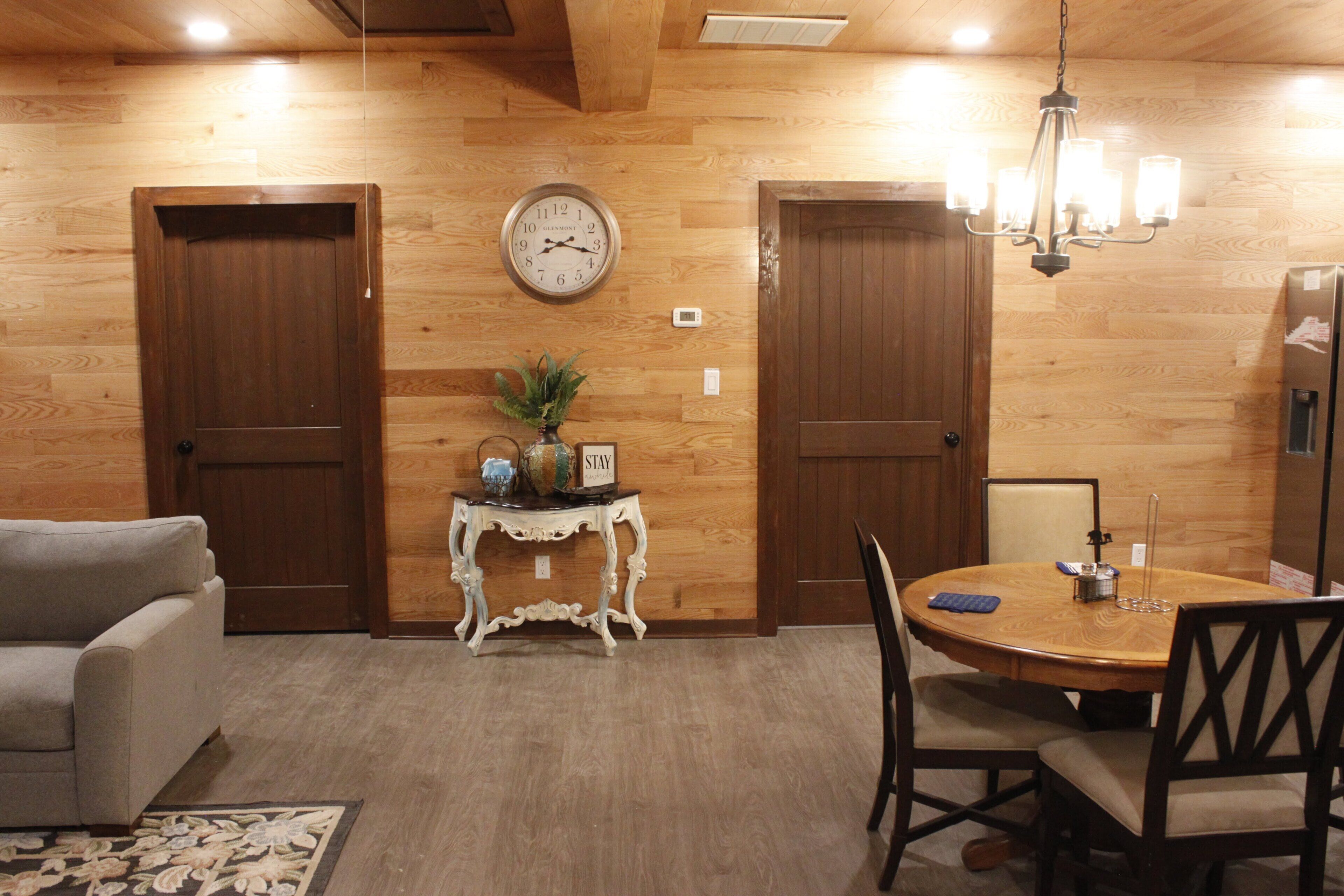 A dining area with a wooden table, chairs, a clock, and a small side table with a plant.