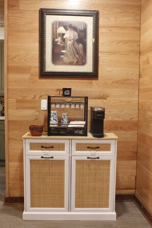 A kitchenette with a coffee maker, a mug, and a framed picture on the wall.