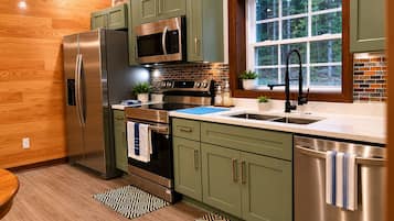 A modern kitchen with stainless steel appliances, a window with a view of trees, and a patterned rug.