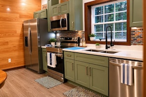 A modern kitchen with stainless steel appliances, a window with a view of trees, and a patterned rug. - Secluded Cabin Retreat - Fast internet - Fire Pit (Summerville)