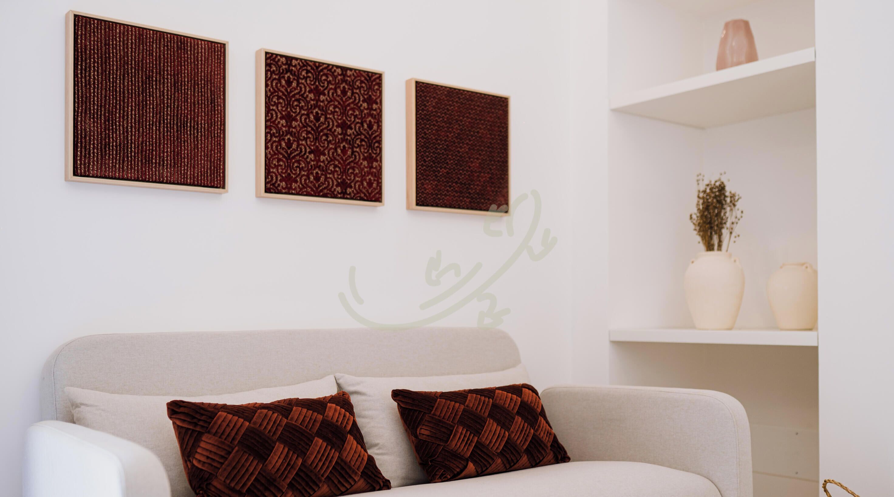 Een moderne woonkamer met een bank, twee decoratieve kussens en drie kunstwerken in lijsten aan de muur.