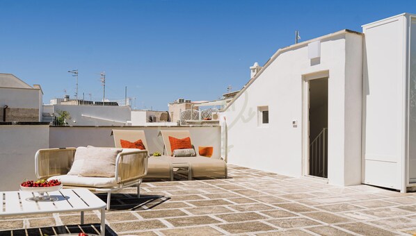 Une terrasse sur le toit avec une chaise blanche, une petite table et un saladier rempli de fruits.