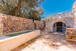 Ein Außenbereich mit Steinmauern, das einen Pool, eine Steinsitzbank und einen überdachten Sitzbereich bietet.
