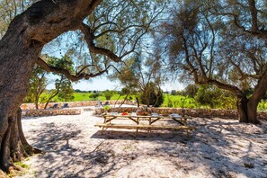 An outdoor dining area with stone walls and a wooden table set for four. - Masseria Grotta Antica 6+2, Emma Villas (Ostuni)