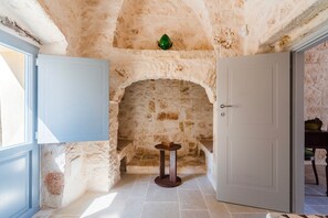 A room with a stone wall, a round wooden table, and a door. - Masseria Grotta Antica 6+2, Emma Villas (Ostuni)