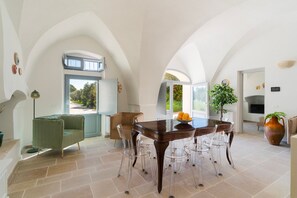 A spacious dining area with a large table and chairs, a green sofa, and a view of the outdoors through a window. - Masseria Grotta Antica 6+2, Emma Villas (Ostuni)