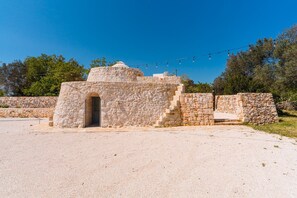 A stone structure with an arched entrance, surrounded by a stone wall and a clear sky. - Masseria Grotta Antica 6+2, Emma Villas (Ostuni)