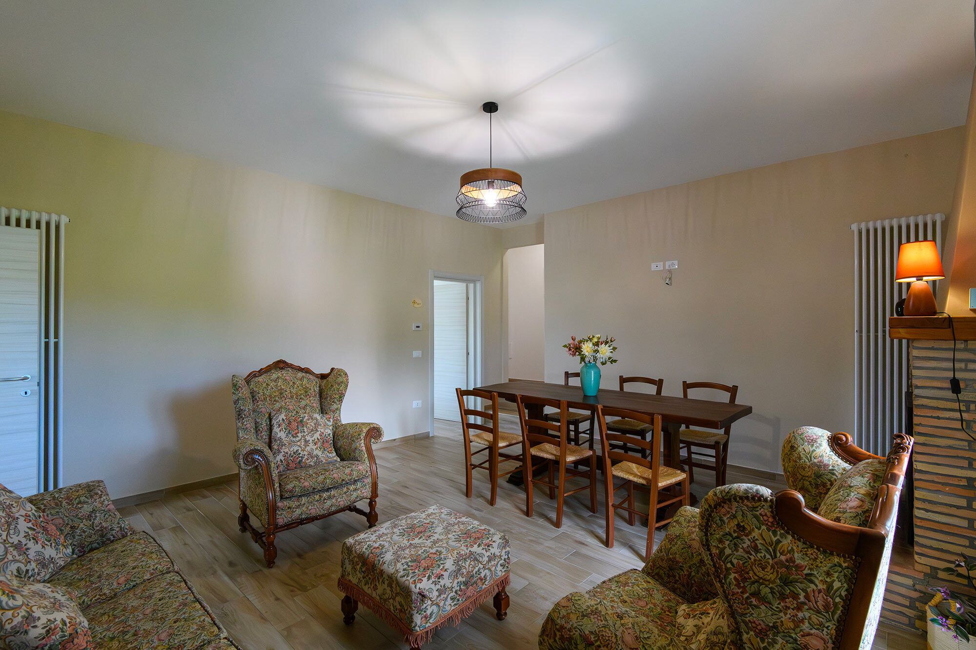 Un coin repas avec une table et des chaises en bois, un fauteuil à motifs floraux et un luminaire suspendu au plafond.