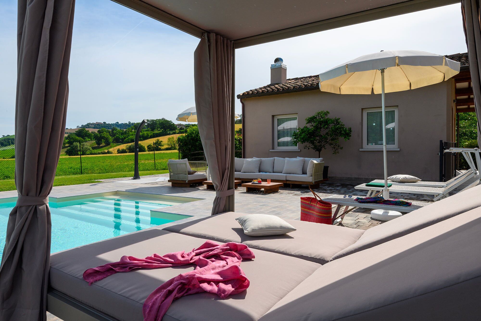Ein Poolbereich mit einer Couch und Liegestühlen, einem Tisch mit einem Getränk und Blick auf ein Haus und die Landschaft.