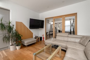 A modern living room with a sofa, a glass coffee table, and a TV mounted on the wall. - GuestReady - Modern Cottage, East Finchley Village (London)
