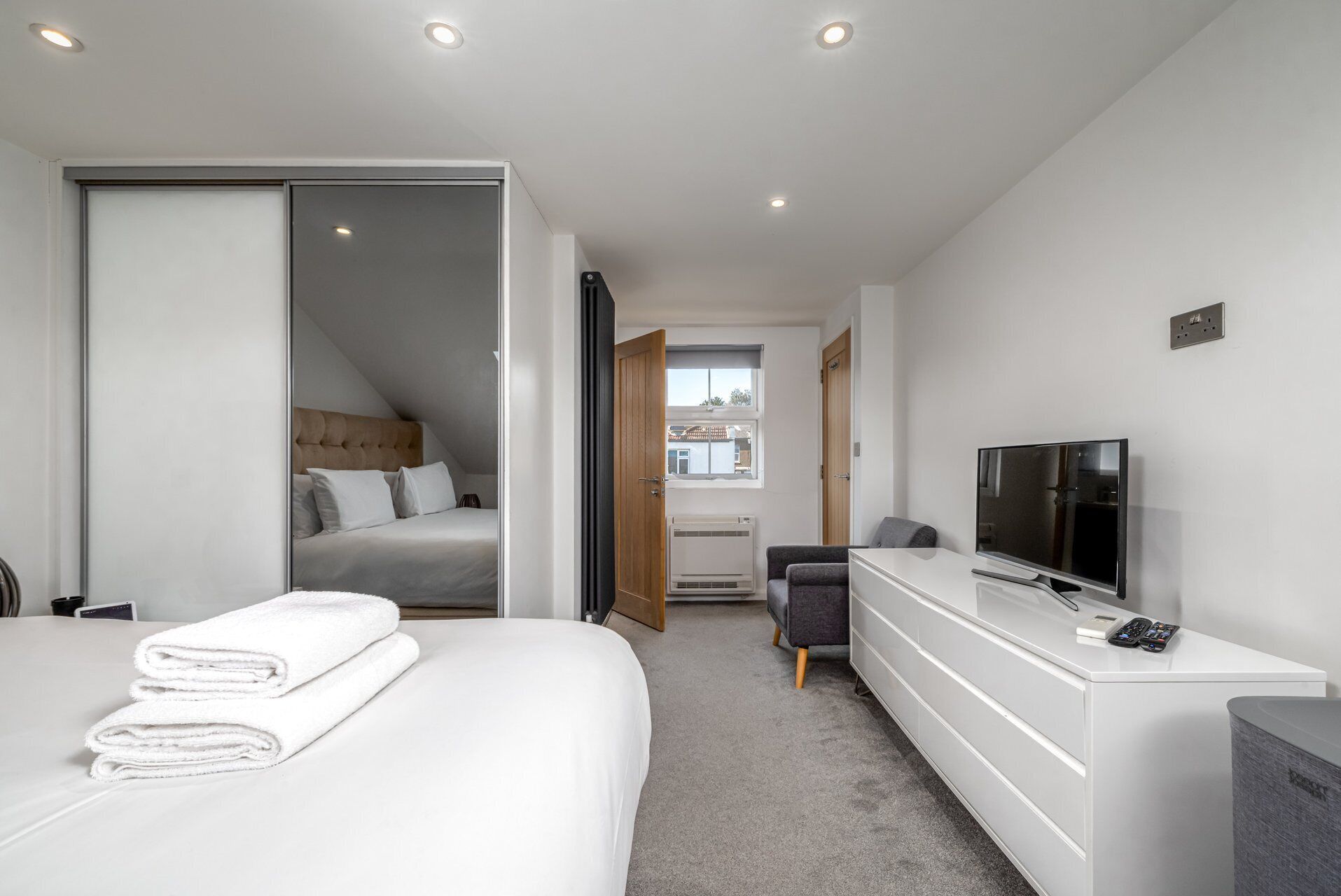 A modern hotel room with a bed, a TV, a desk, and a window.