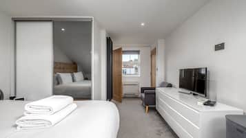 A modern hotel room with a bed, a TV, a desk, and a window.