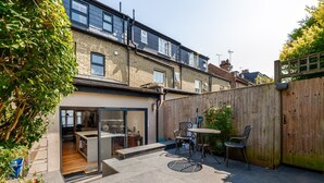 En bostadsträdgård med en uteplats, ett trästaket och en liten trädgårdsanläggning.