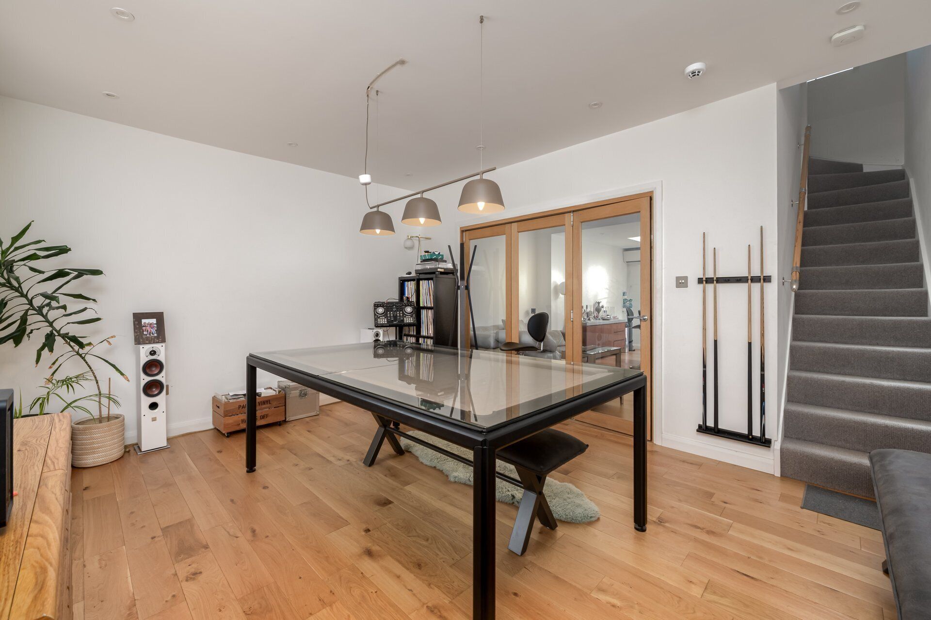 A modern dining area with a glass table, wooden flooring, and a staircase.