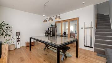 A modern dining area with a glass table, wooden flooring, and a staircase.