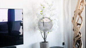 Uma sala de estar moderna com uma TV de tela plana na parede, um vaso alto com flores brancas, um alto-falante preto e uma escultura de madeira única.