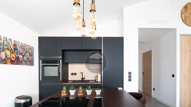 Uma cozinha moderna com ilha central, forno embutido e luminárias pendentes.