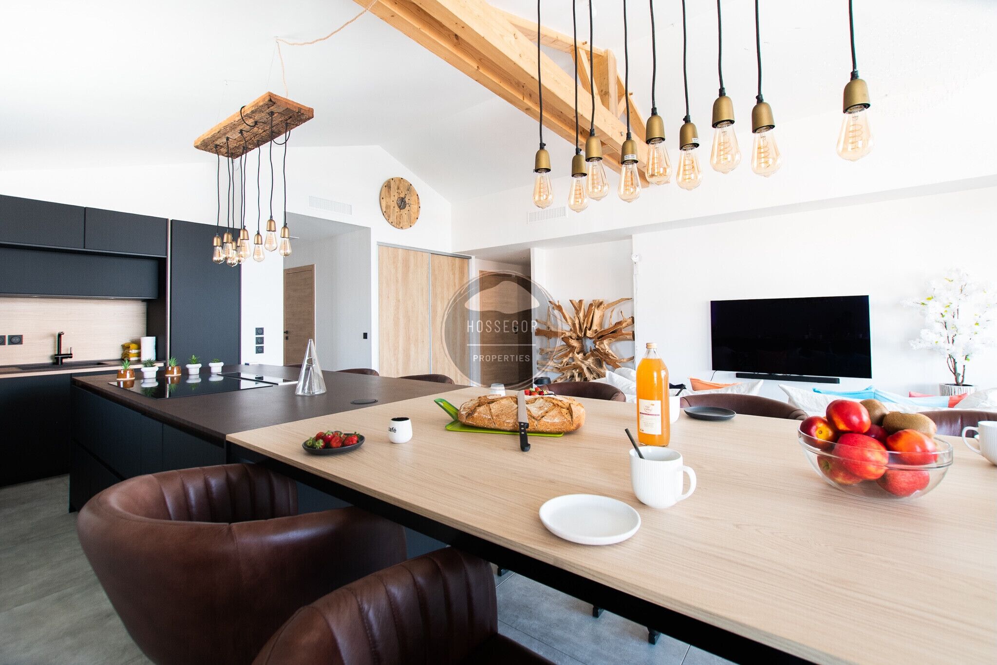 Una cocina moderna con una isla central, lámparas colgantes y un televisor de pantalla plana.