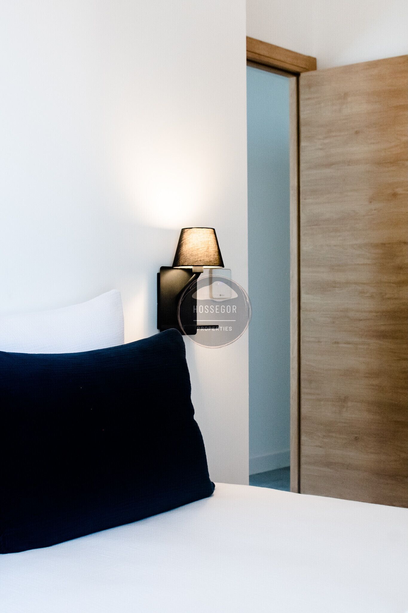 Ett hotellrum med en säng, en vägglampa och en garderob.