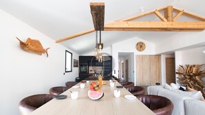 Uma sala de jantar moderna com uma mesa comprida, cadeiras de couro e um lustre central.