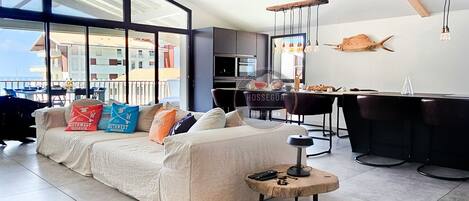 A modern living room with a sofa, a coffee table, and a dining area with chairs and a bar.