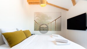 A bedroom with a bed, pillows, a painting, a television, and a ceiling fan.