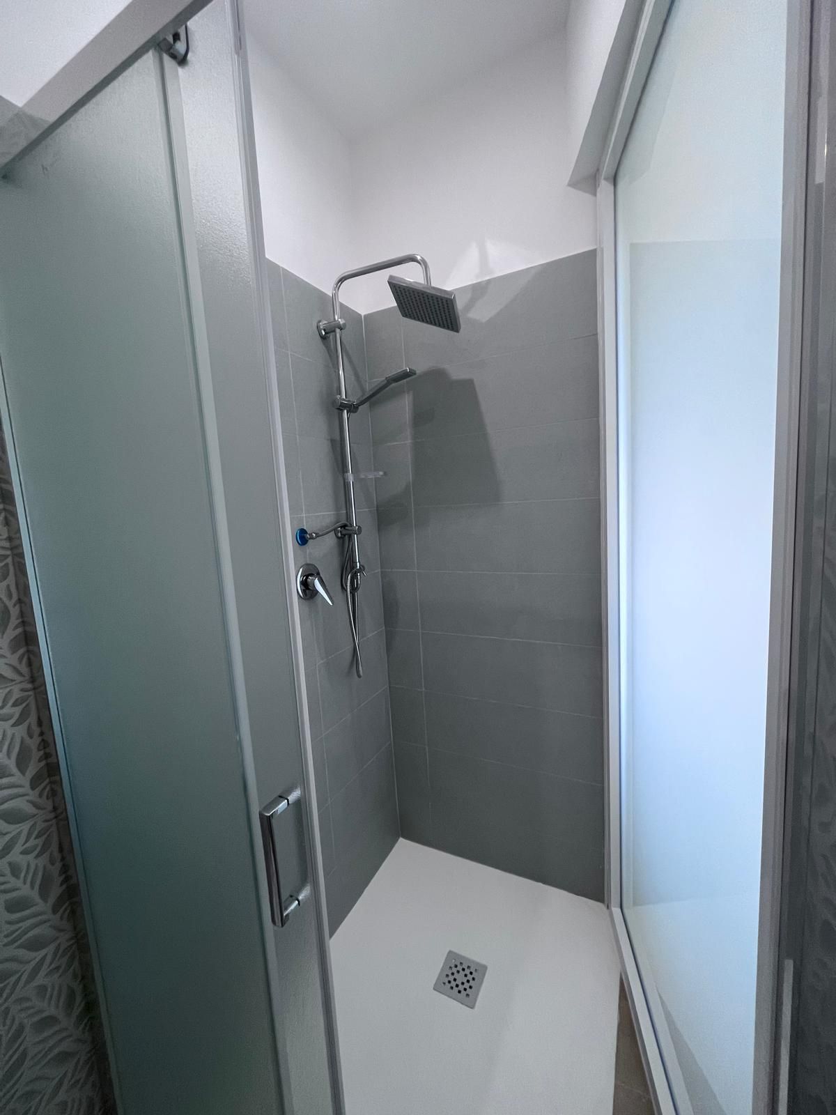 Una ducha moderna con cabezal de ducha de mano y un cabezal de ducha tipo lluvia empotrado en la pared, puerta de vidrio y suelo de baldosas.