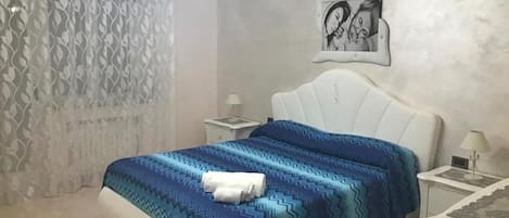A bedroom with a bed, a nightstand, a lamp, a wall art piece, and a patterned curtain.