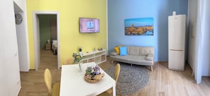 Ein modernes Wohnzimmer mit einer Couch, einem Esstisch mit Stühlen, einem Fernseher und einem Kühlschrank.