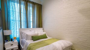 Et hotelværelse med en seng, et natbord, en lampe og et vindue med gardiner.