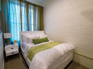 Une chambre d’hôtel avec un lit, une table de chevet, une lampe et une fenêtre avec des rideaux.