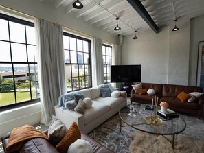 Un salon moderne avec une grande fenêtre, un canapé, une table basse et un téléviseur.