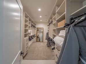 Un dressing accessible sans porte, doté de nombreuses étagères et d’un espace pour suspendre les vêtements, ainsi que d’un sol recouvert de moquette et d’un miroir.