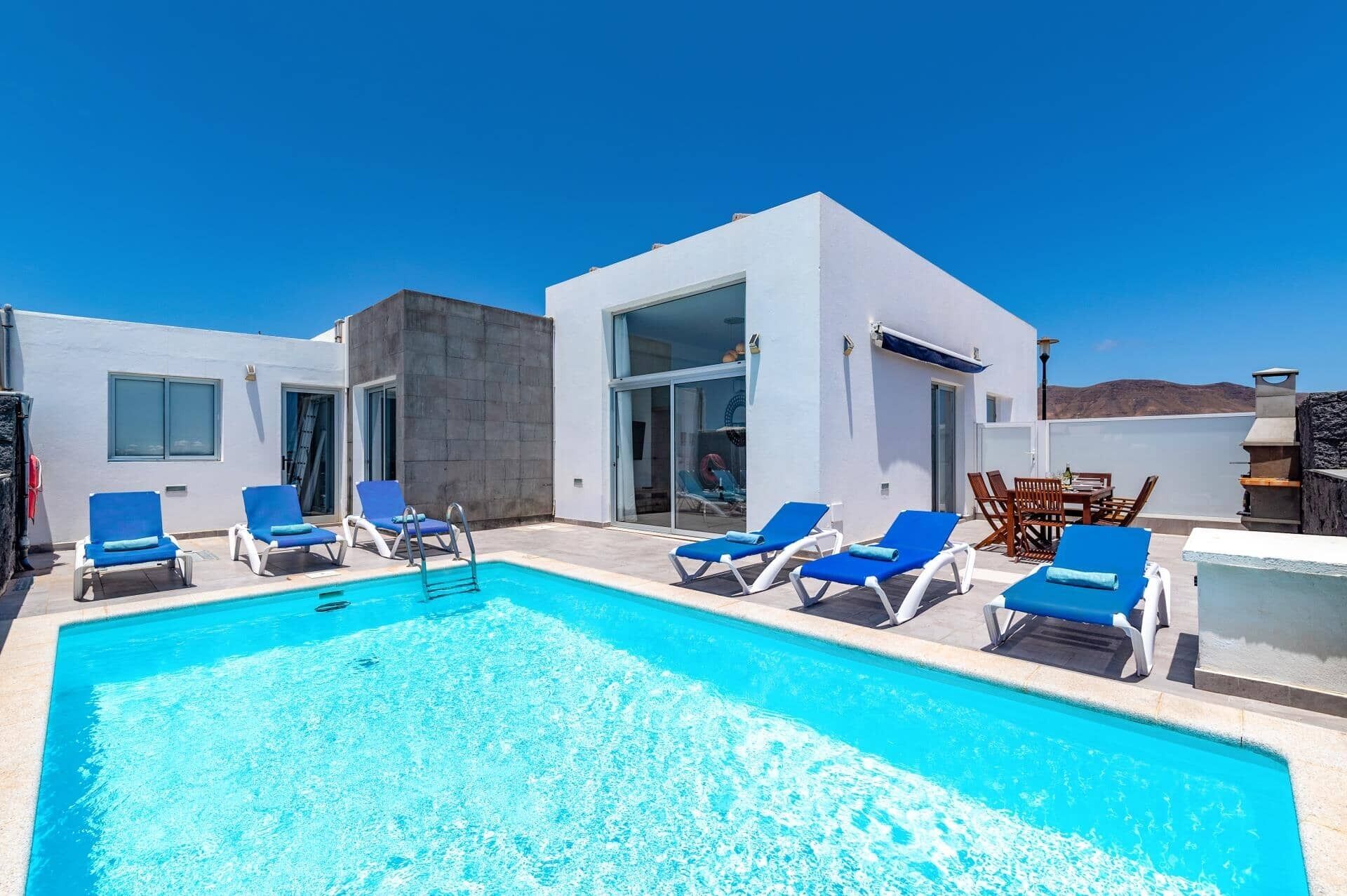 Un espace piscine aménagé sur le toit, avec des chaises longues bleues et un ciel d’un bleu limpide.
