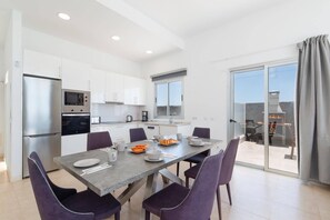 A modern kitchen with a dining area, a large window, and a sliding glass door leading to an outdoor patio. - Villa Blue Horizon by Villa Plus (Playa Blanca)